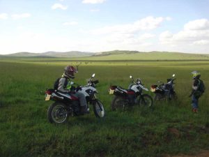una persona y 3 motos en el pasto con una montaña de fondo