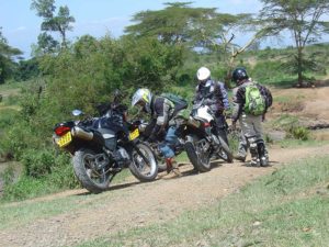 3 personas reparando una moto sobre camino de tierra